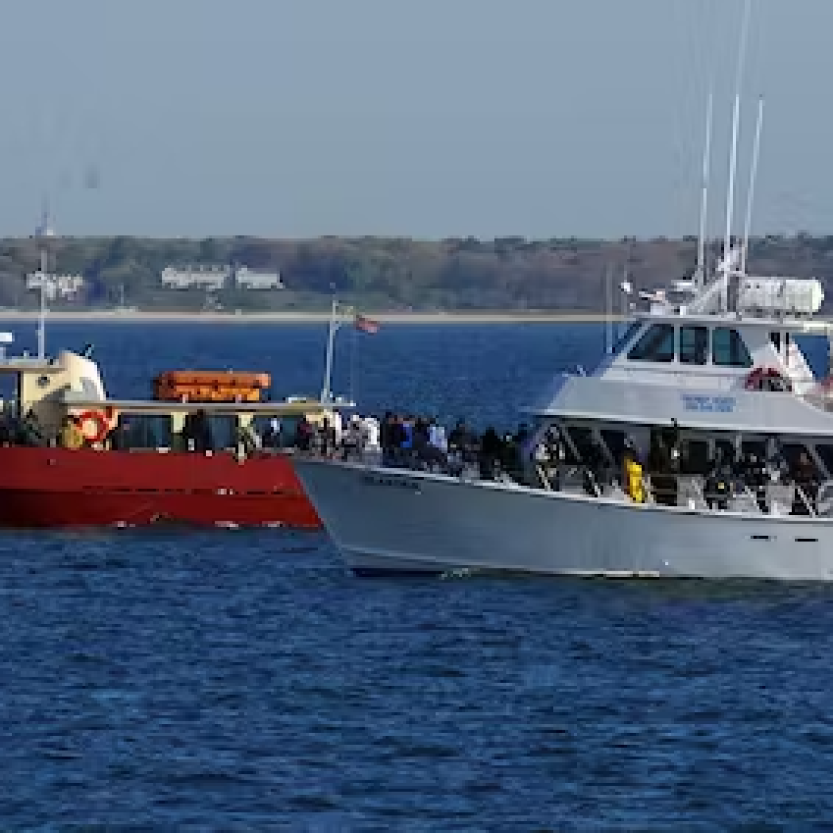 Two boats, one red and one white, on calm water with many people visible on board.