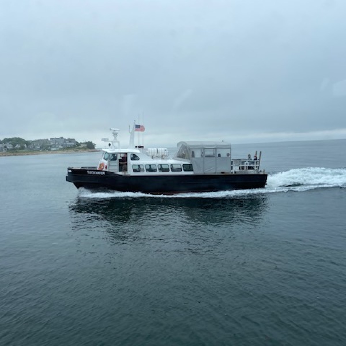 Boat with American flag on calm water near coastline on a cloudy day.