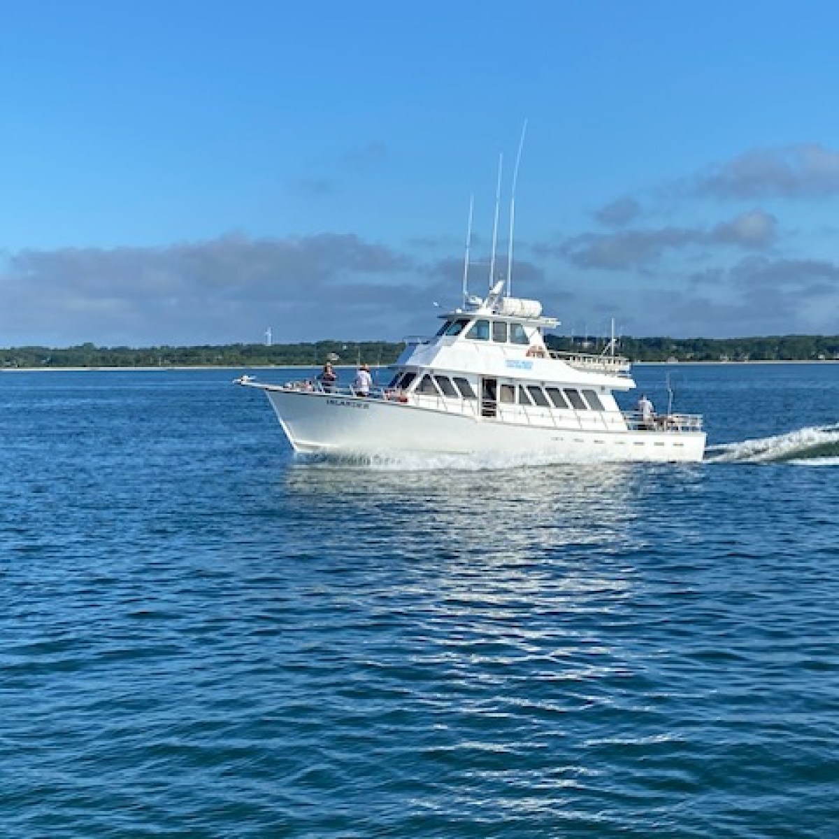 White boat sailing on calm blue water near a distant shoreline under a clear sky.