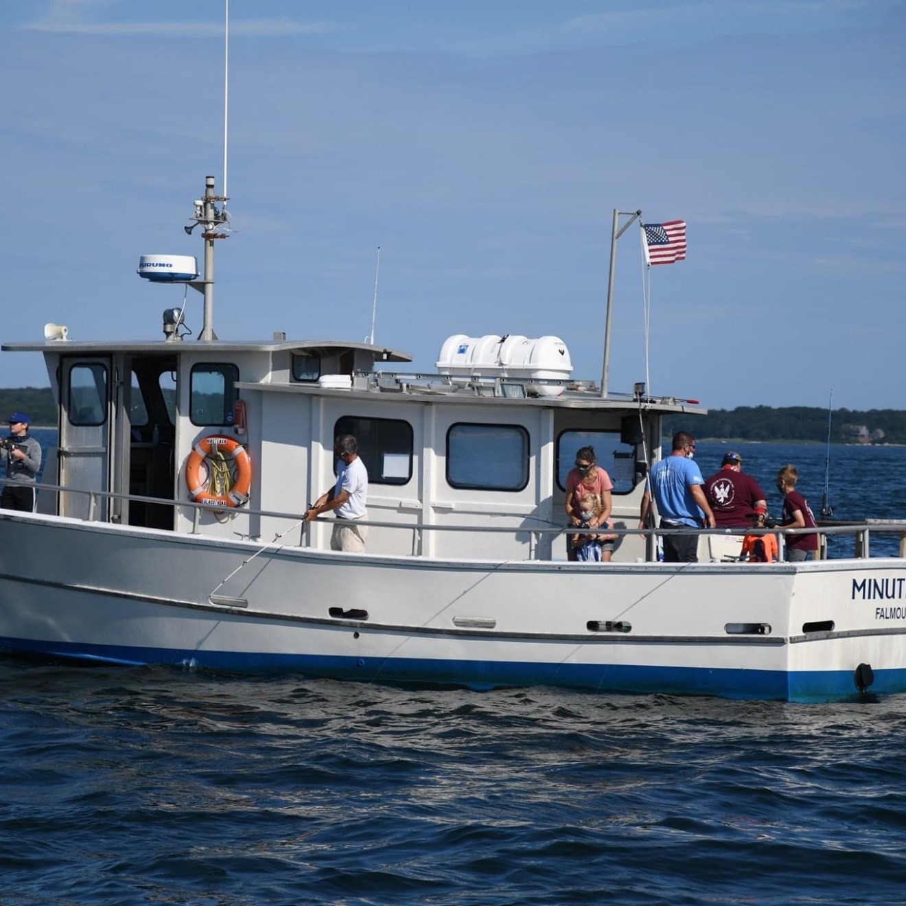 A group of people on a white boat with an American flag on a sunny day.