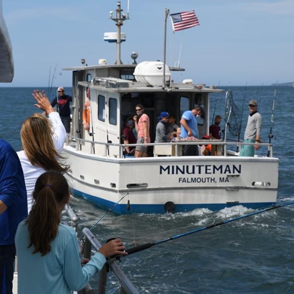 People waving from a boat named Minuteman on the ocean.
