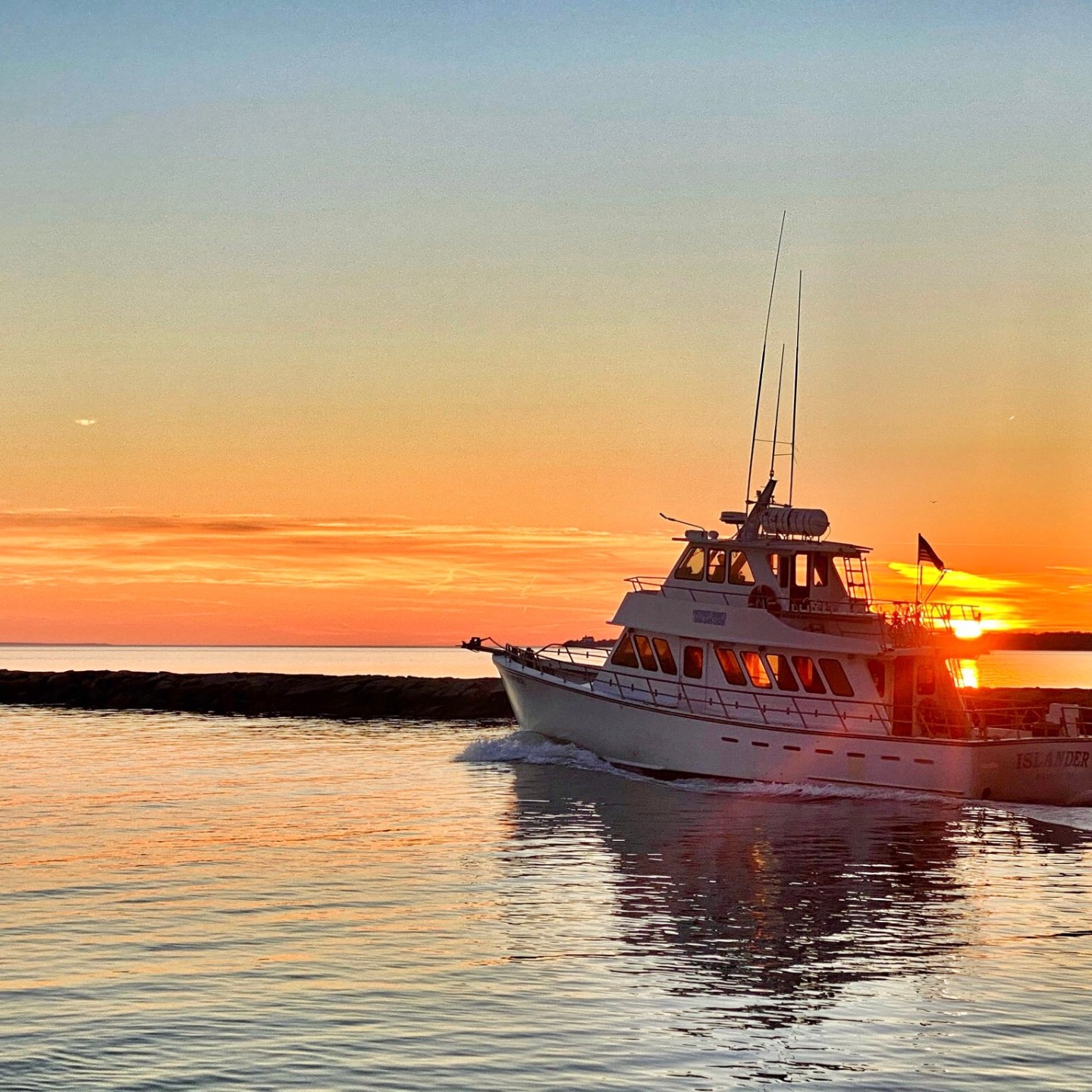 Boat sailing on calm water at sunset with a lighthouse.