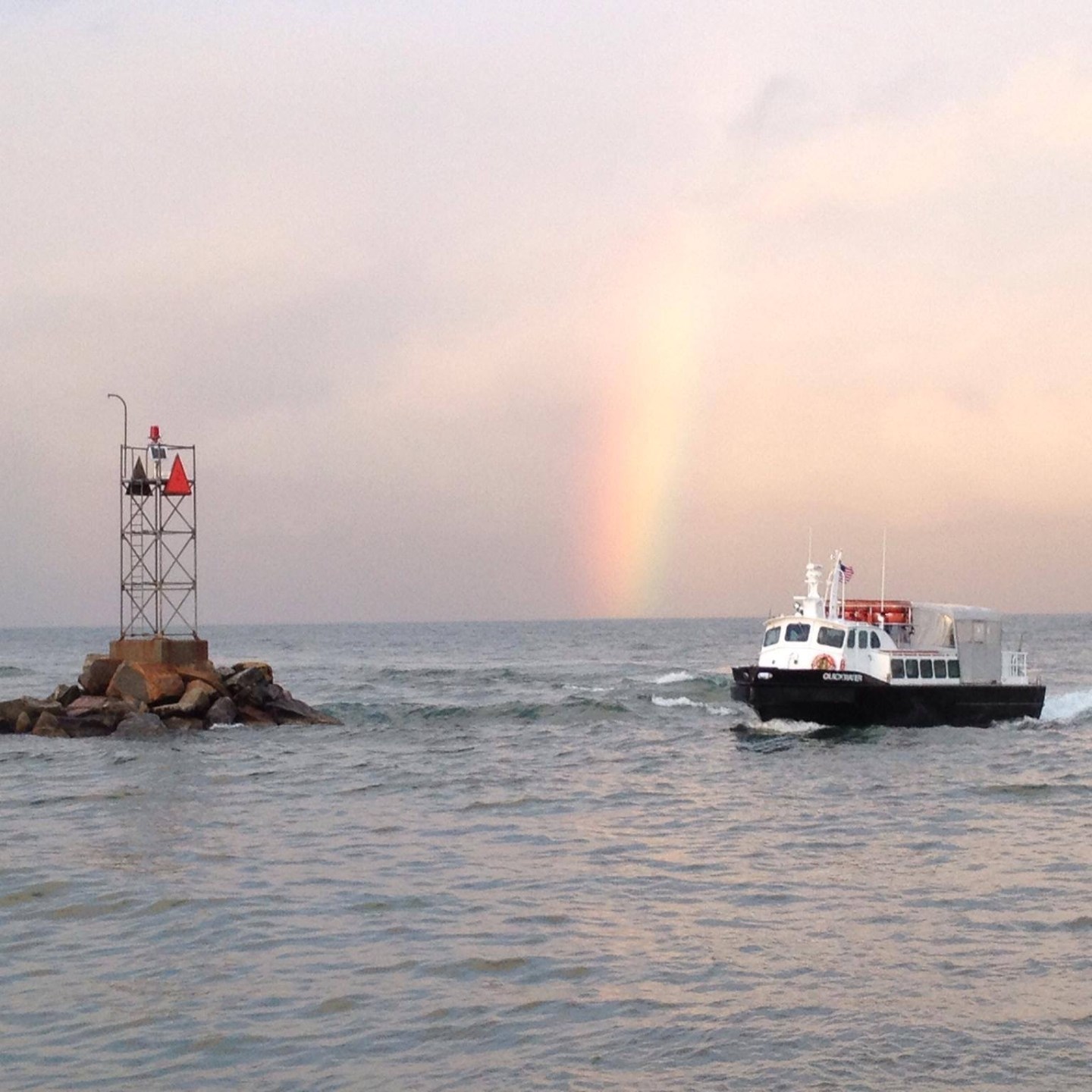 Boat near rocky structure with a rainbow over the ocean.