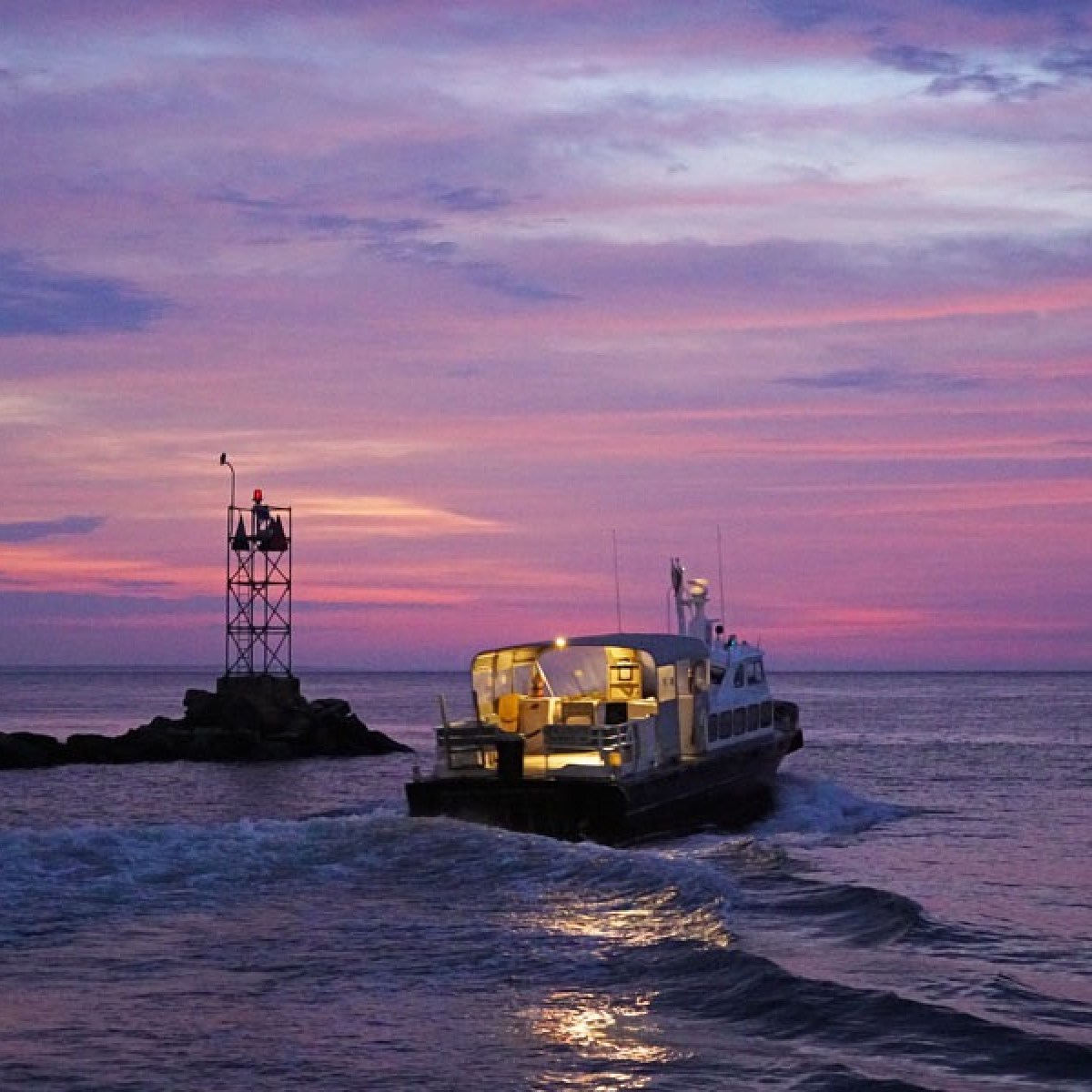 Boat leaves shore under vibrant purple and pink sunset sky.