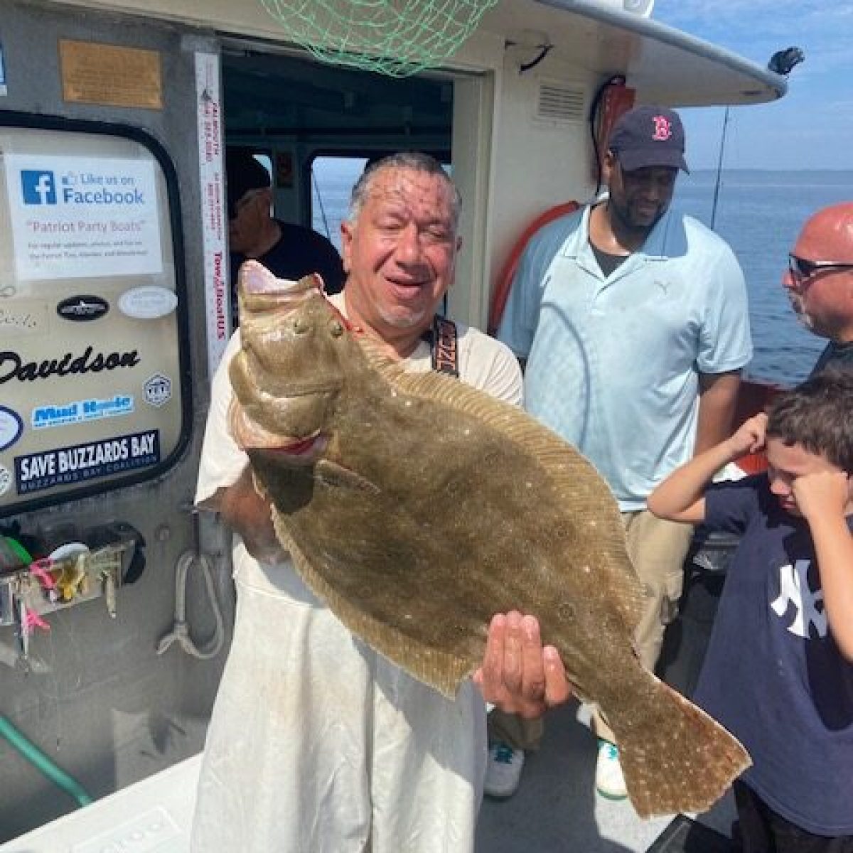 Man proudly holds a large fish on a boat with people around him.