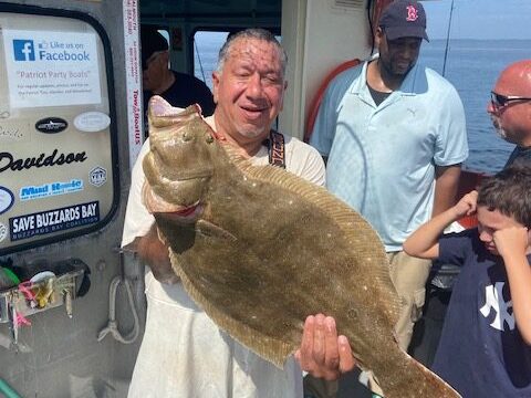 Man proudly holds a large fish on a boat with people around him.