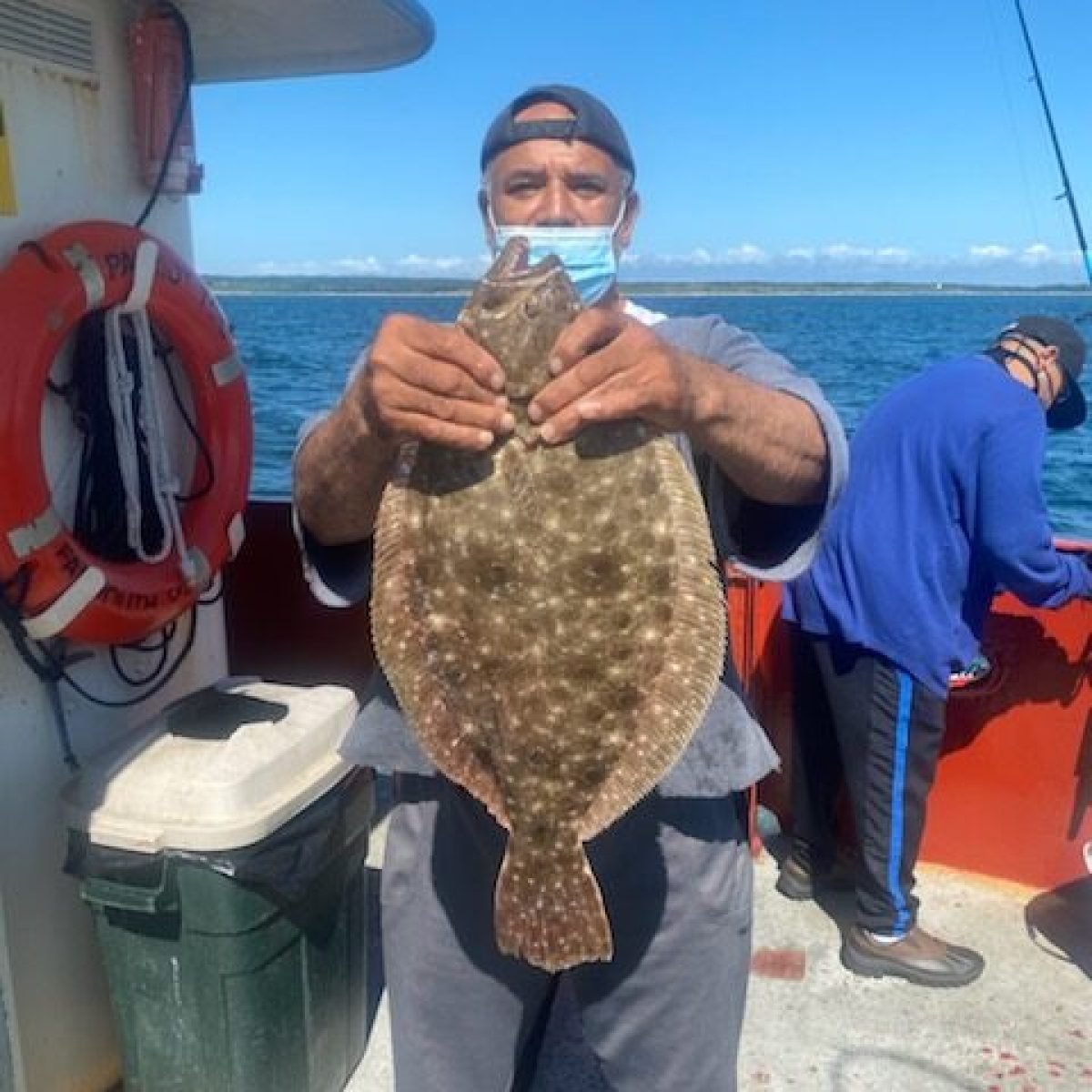Person holding a large flat fish on a boat with a lifebuoy in the background.