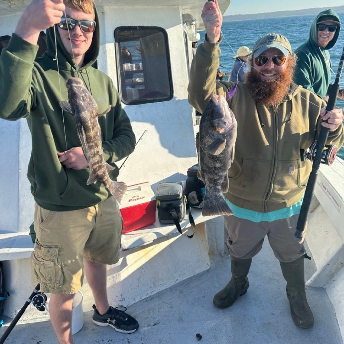 Two people on a boat holding fish they caught, smiling.