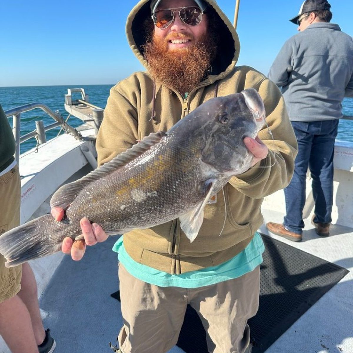 Smiling person in a hoodie holding a large fish on a boat.