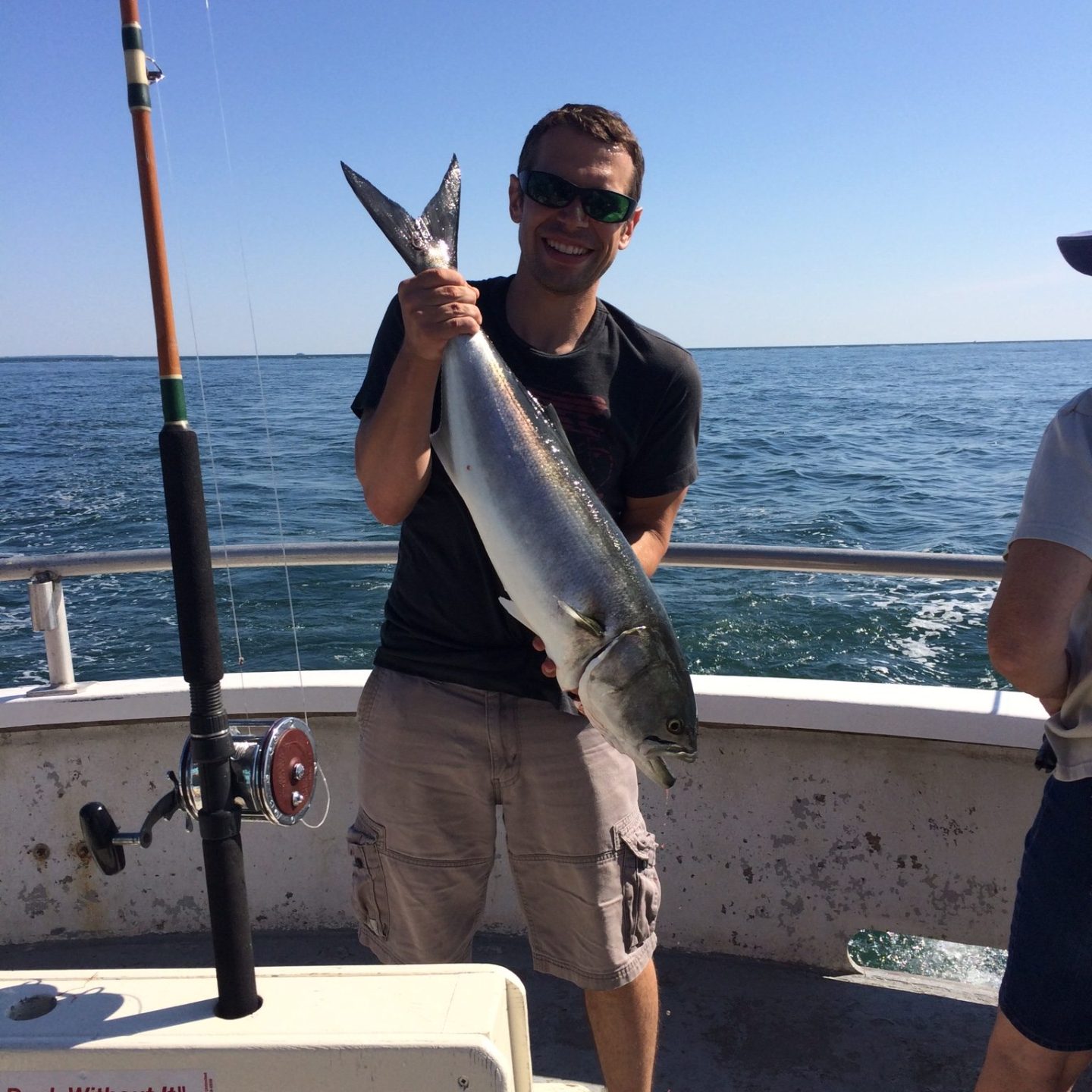 Person on boat holding a large fish with fishing rod nearby.