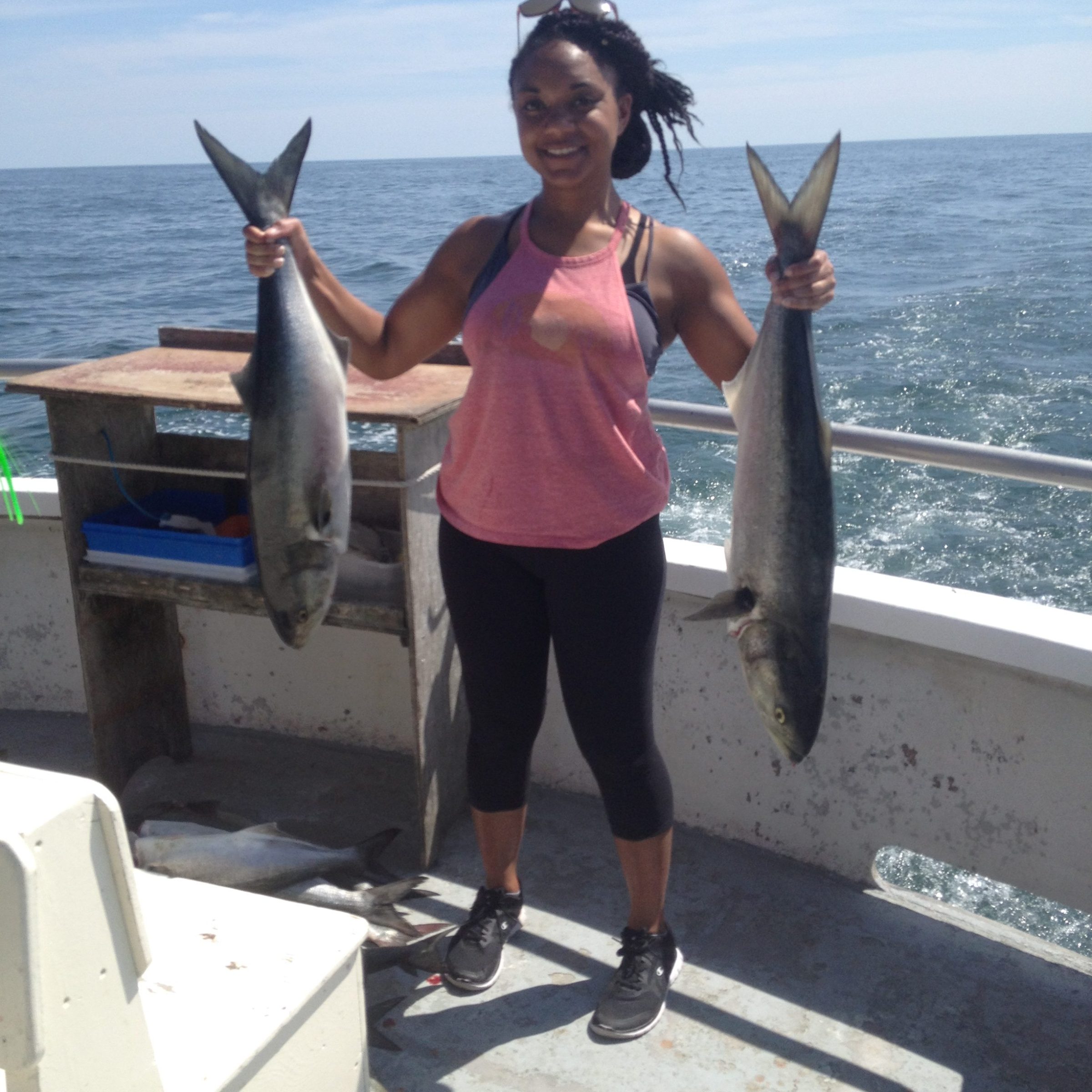 Person on boat holding two large fish, ocean in background.