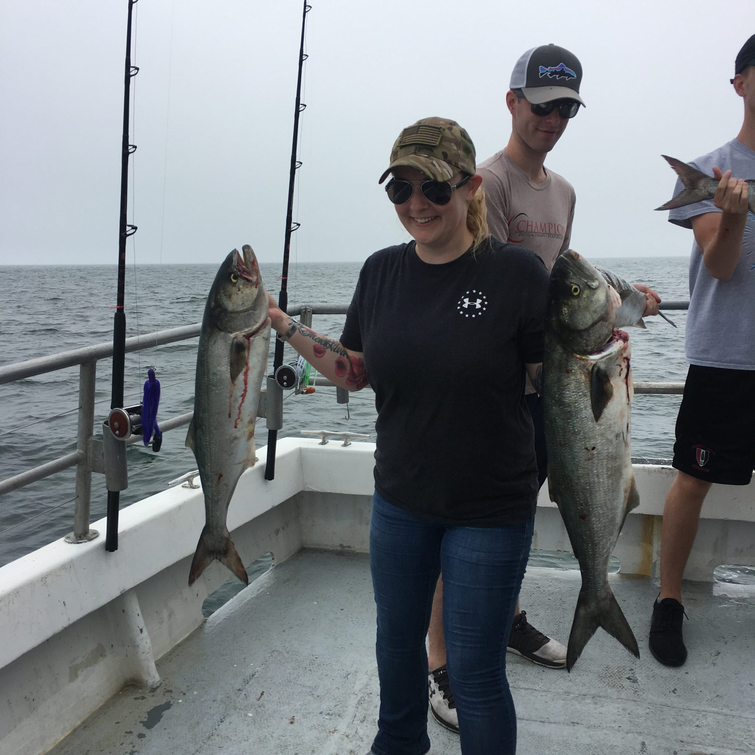 Person on boat holding two large fish with another person in the background.