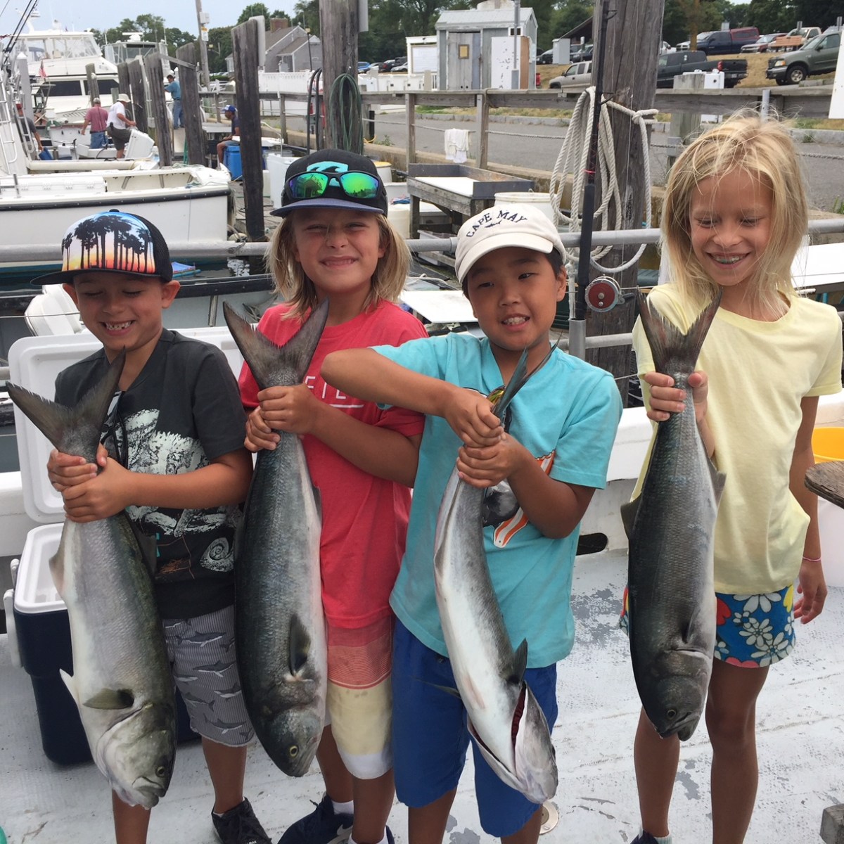 Four children holding large fish on a boat at a marina.