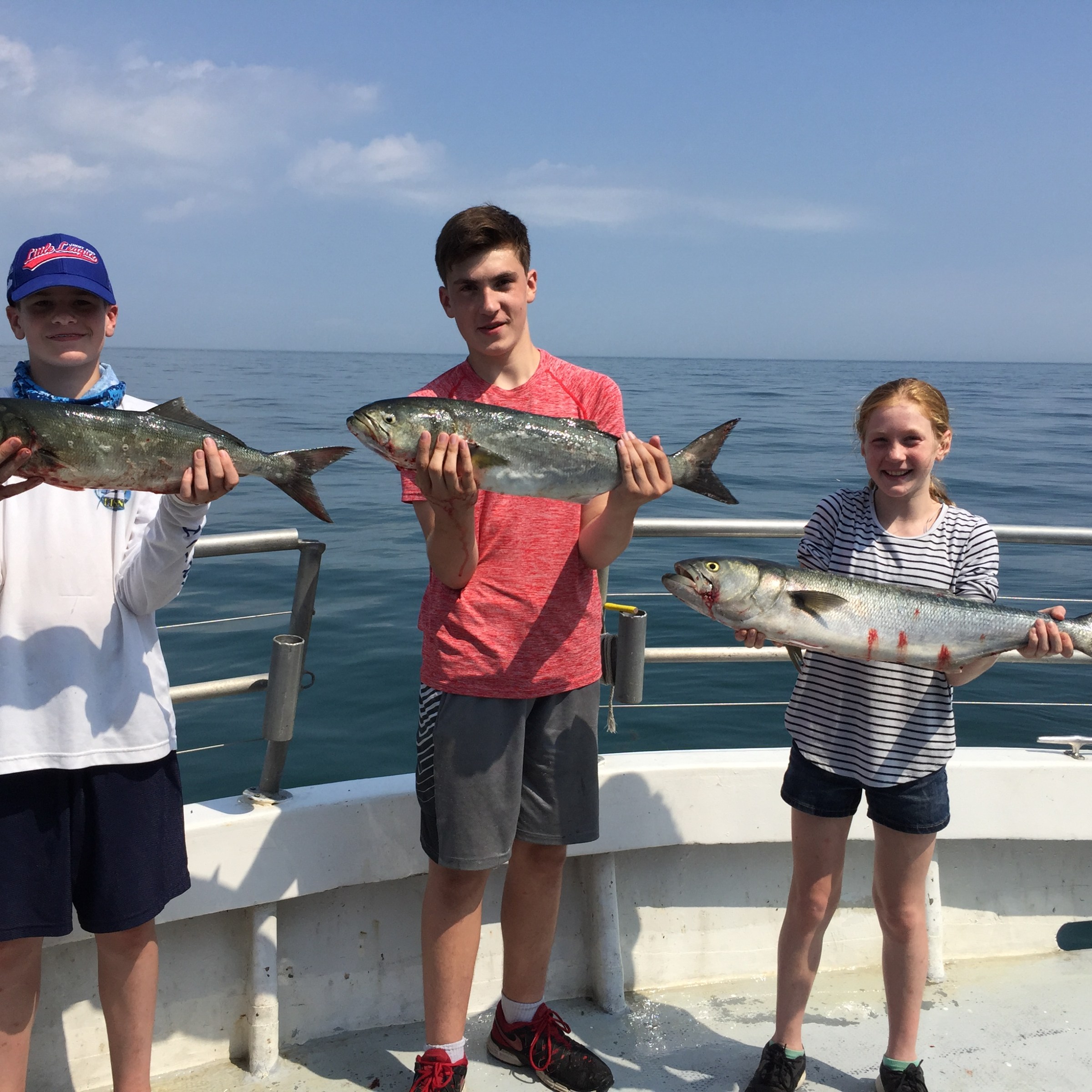Three kids holding fish on a boat with ocean background.