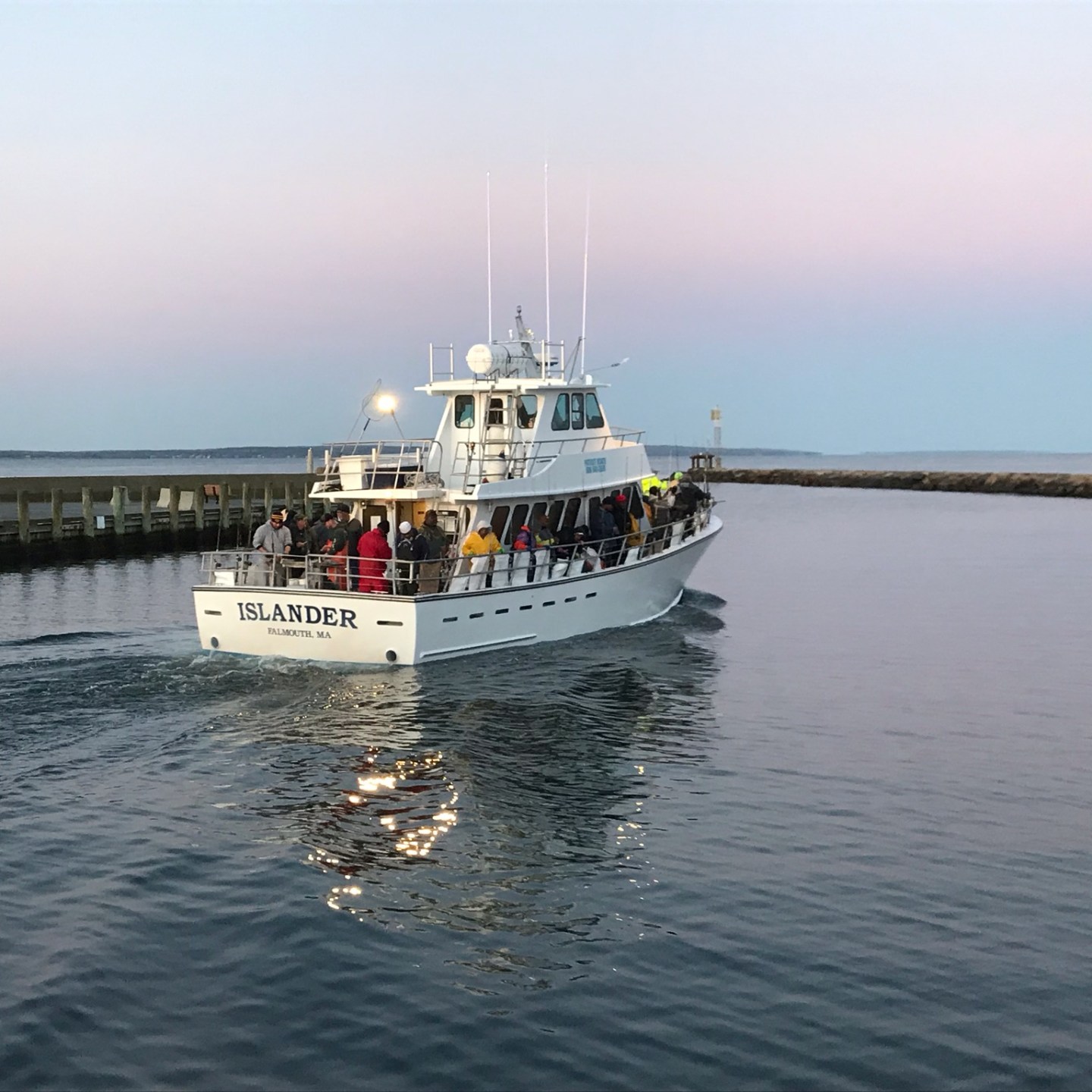 A passenger boat named Islander sailing on calm water near a pier at dusk.