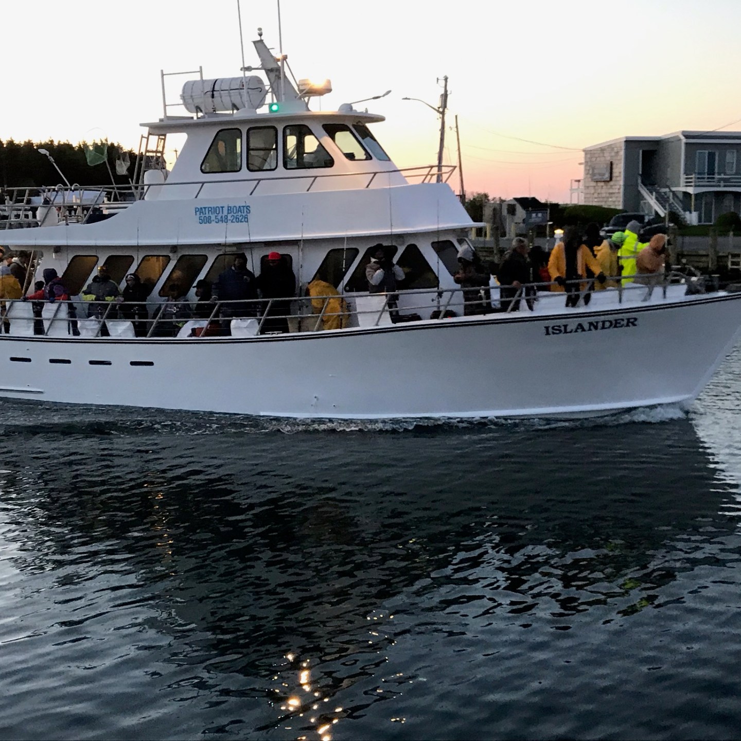 Boat named 'Islander' on water with people on deck at dusk.