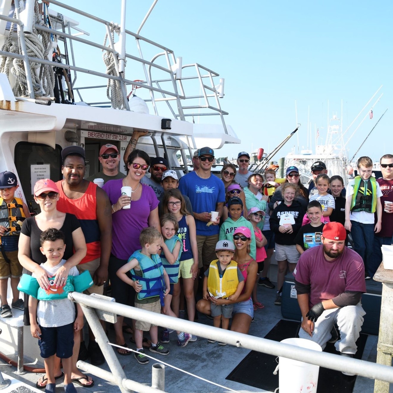 Group of people on a boat, smiling and posing for a photo on a sunny day.