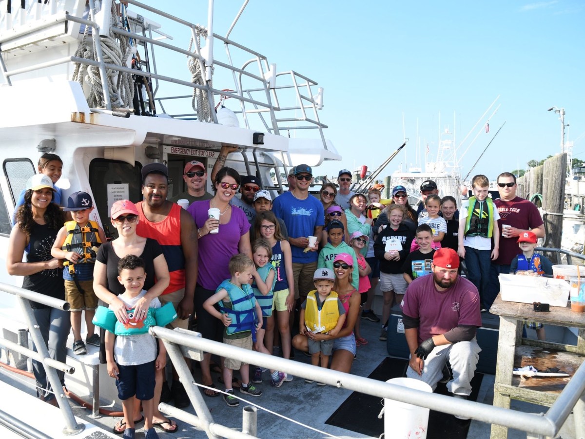 Group of people on a boat, smiling and posing for a photo on a sunny day.