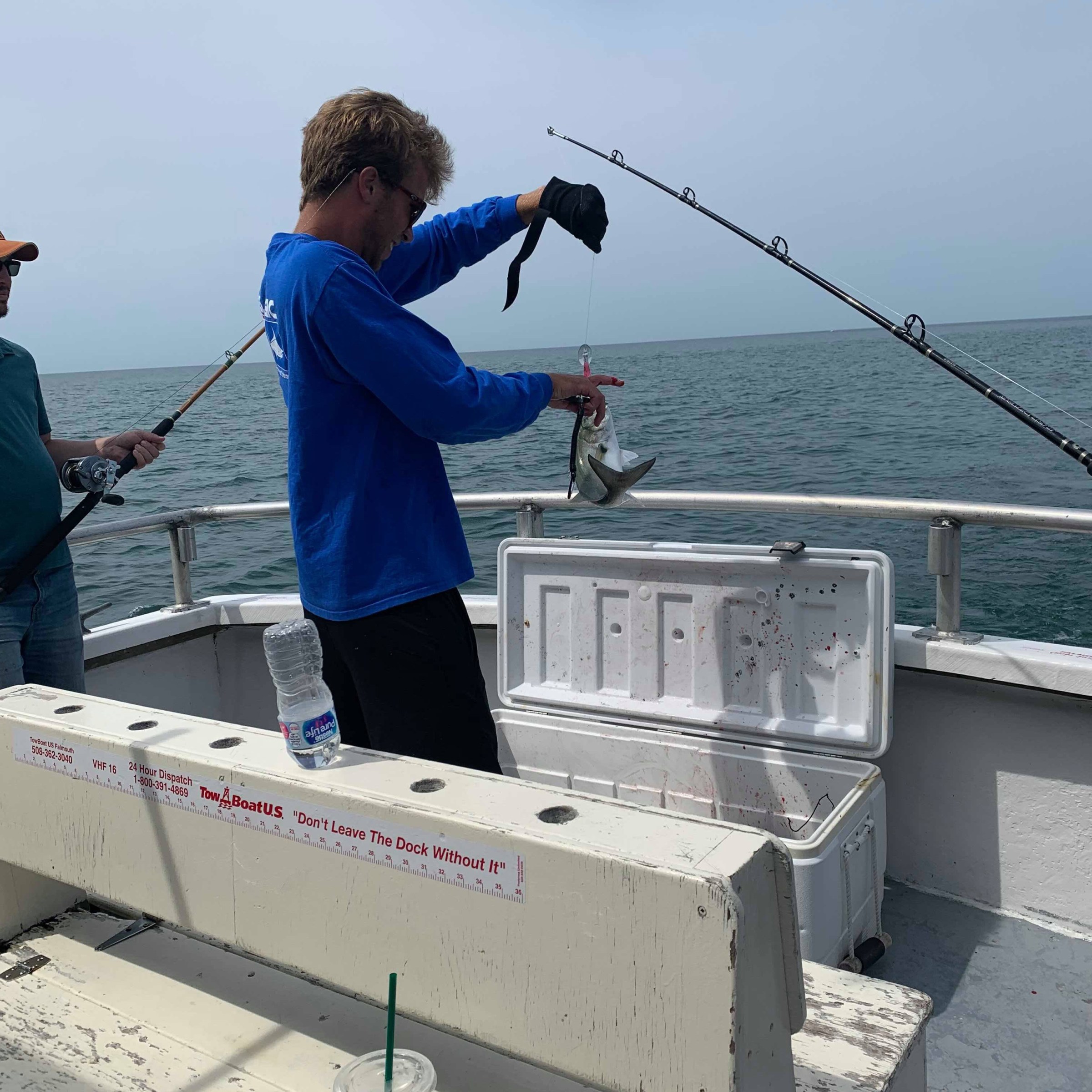 Person holding fish on boat with cooler and fishing rods nearby.