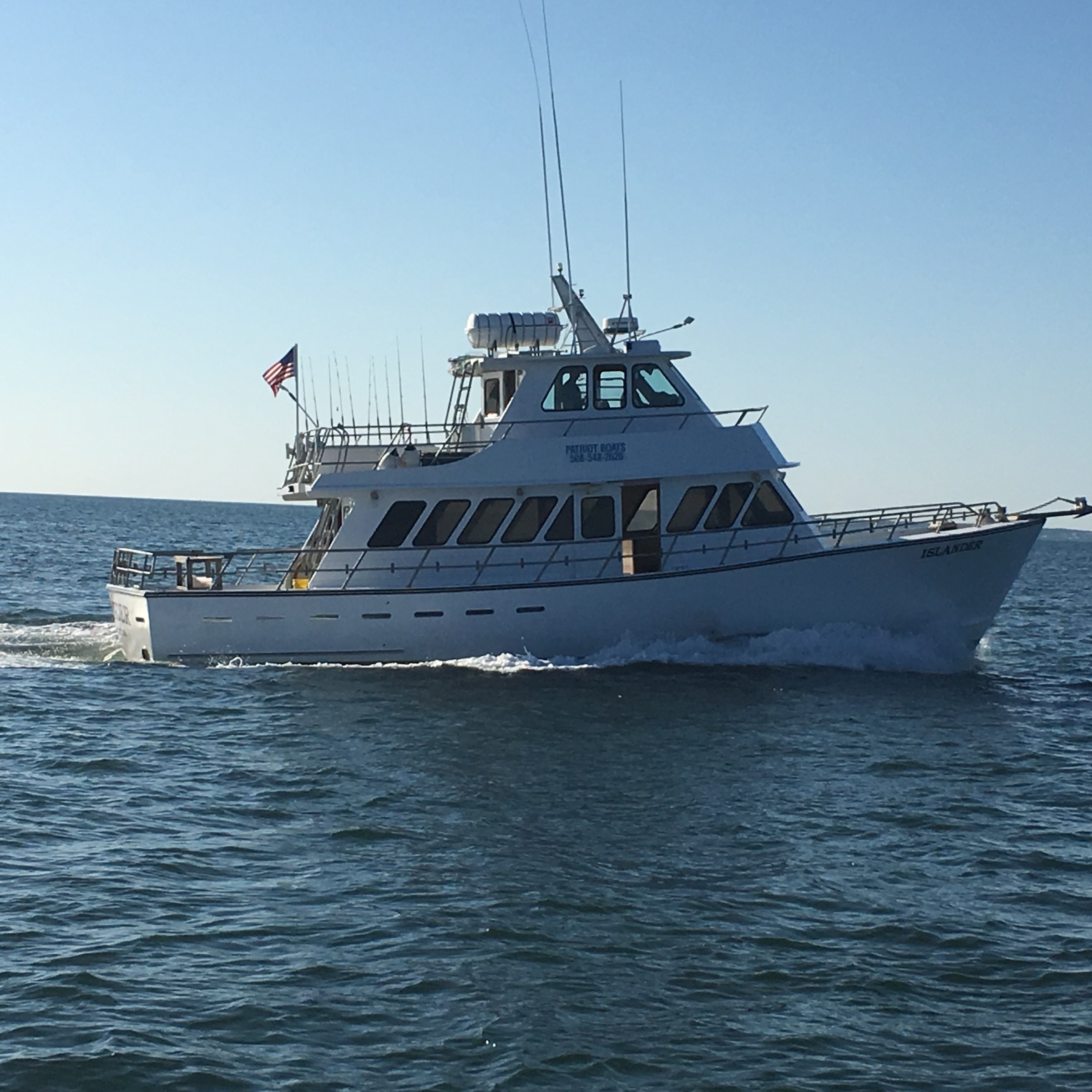 A white fishing boat sails on calm ocean waters under a clear blue sky.