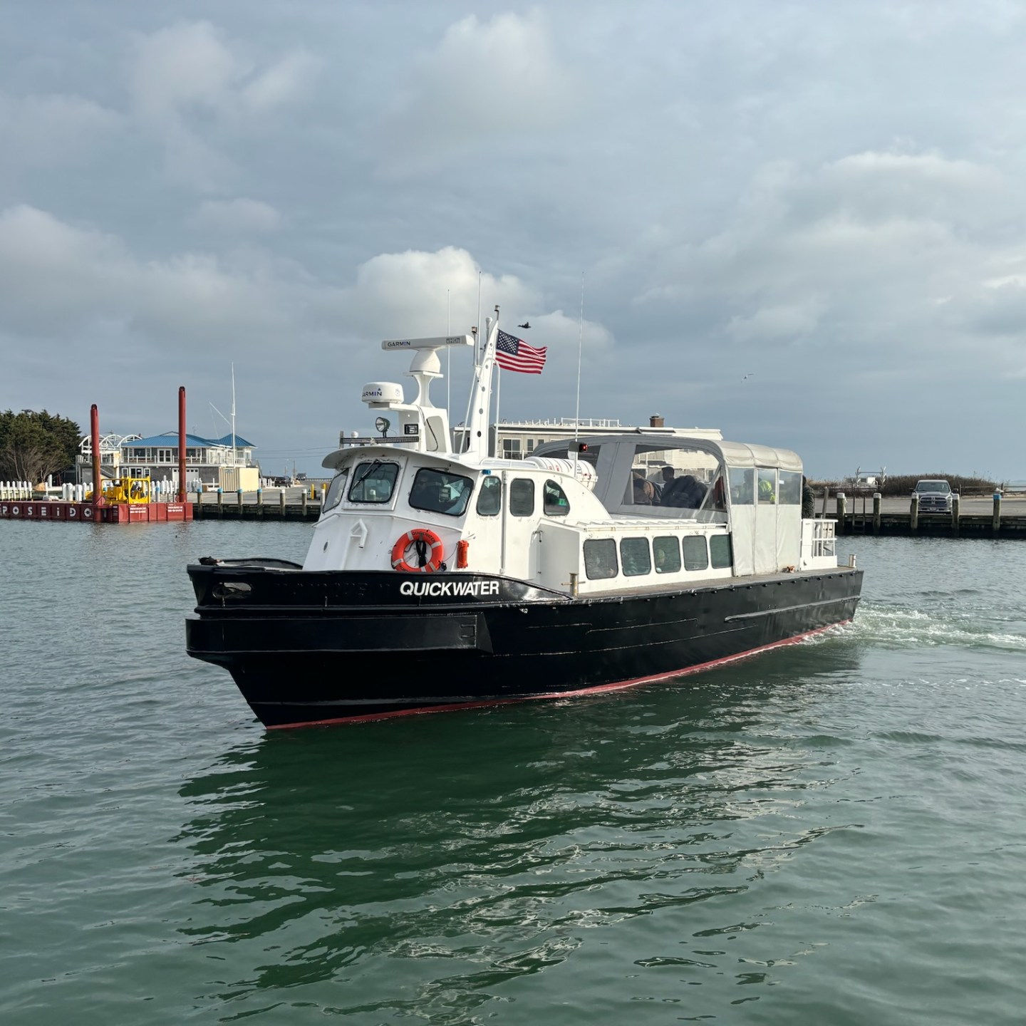 Small ferryboat on water with American flag, cloudy sky.