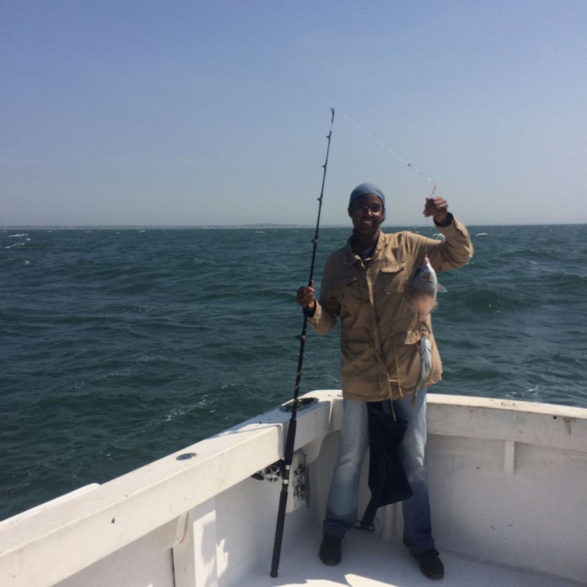 Person holding a fish on a boat in a vast ocean under a clear sky.