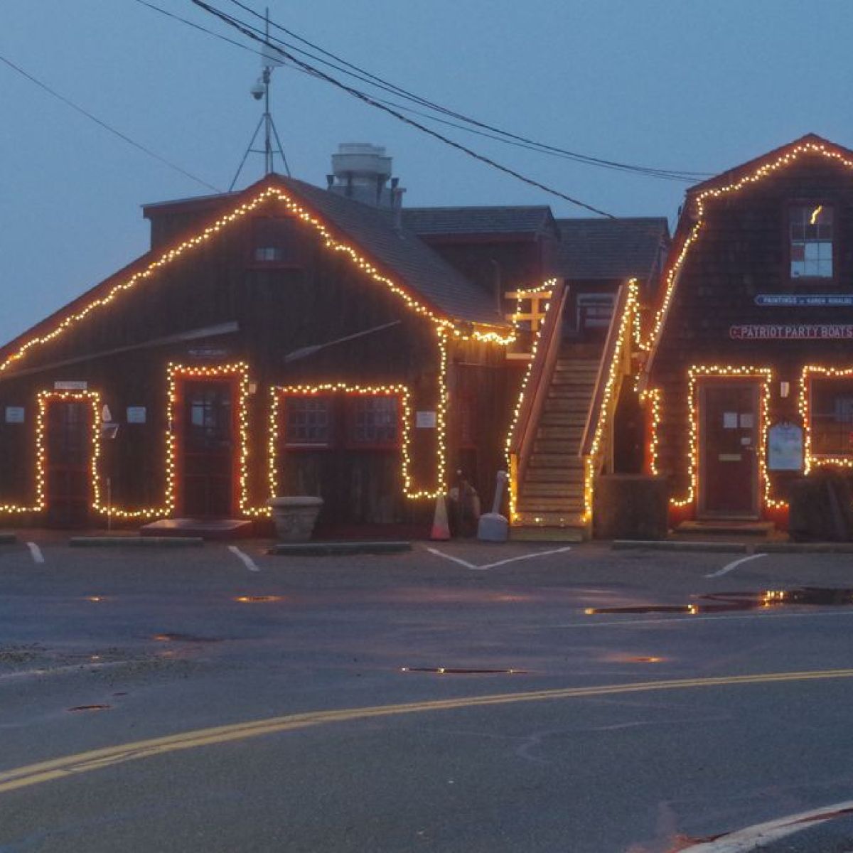 Two wooden buildings with Christmas lights on a cloudy day.