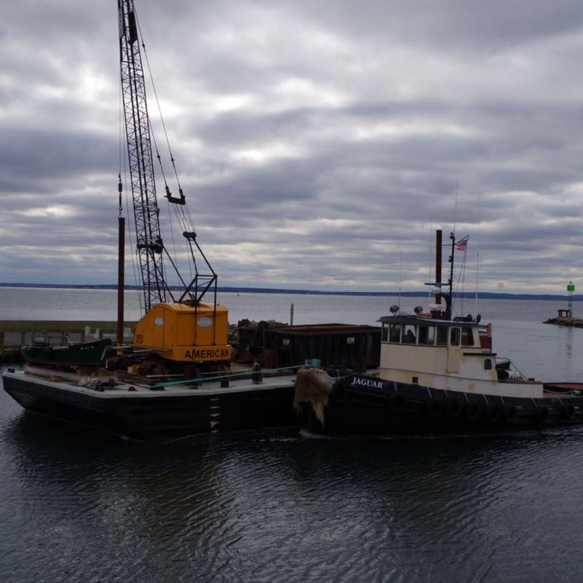 Barge and tugboat with crane on cloudy waterway.