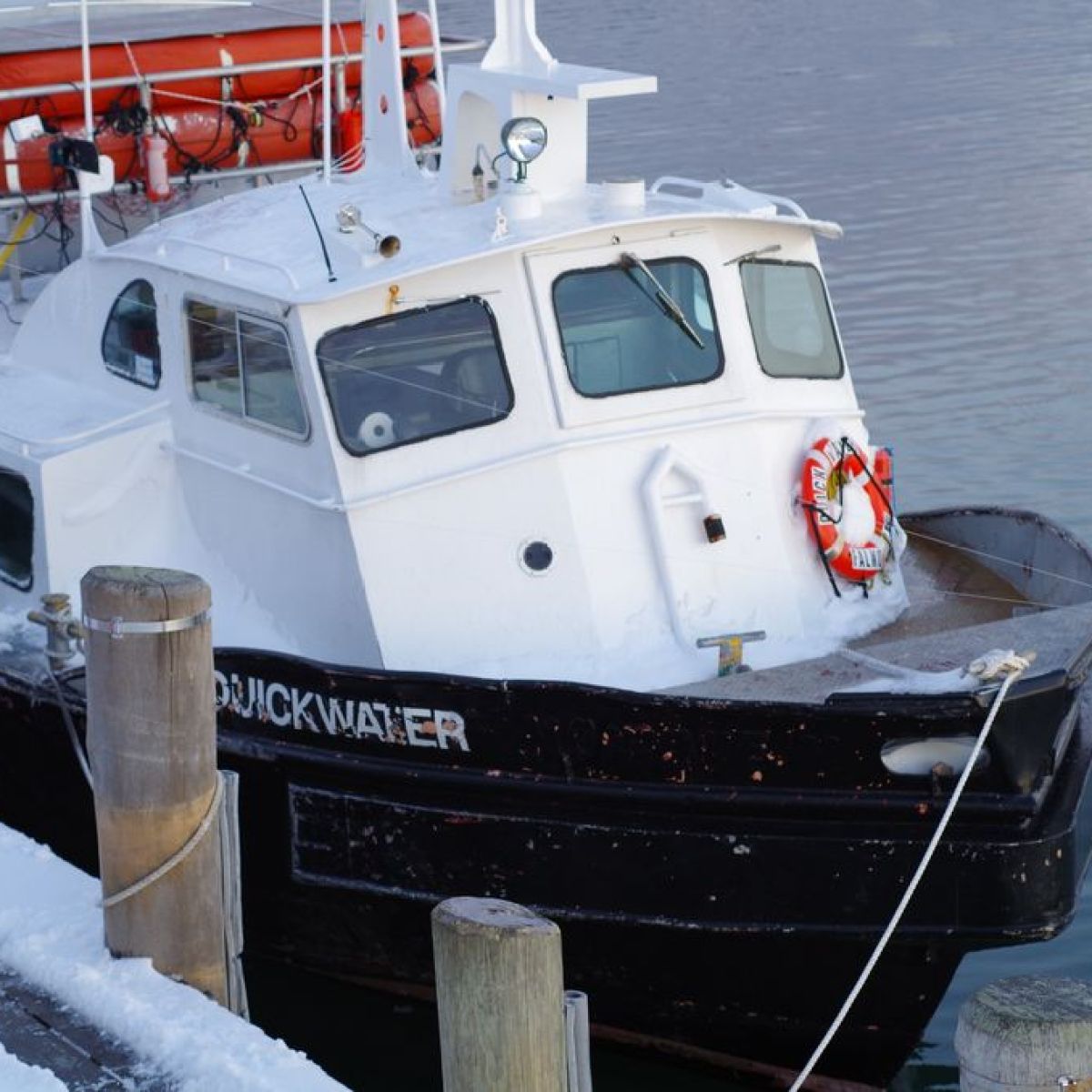 Small boat docked at snowy pier with lifebuoy and orange ring buoys on roof.