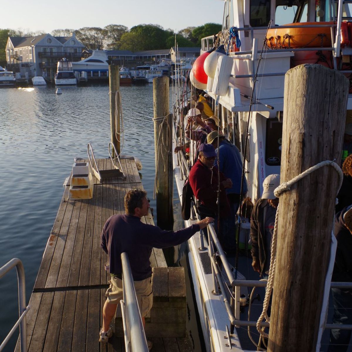 People boarding a boat at a wooden dock during sunset.
