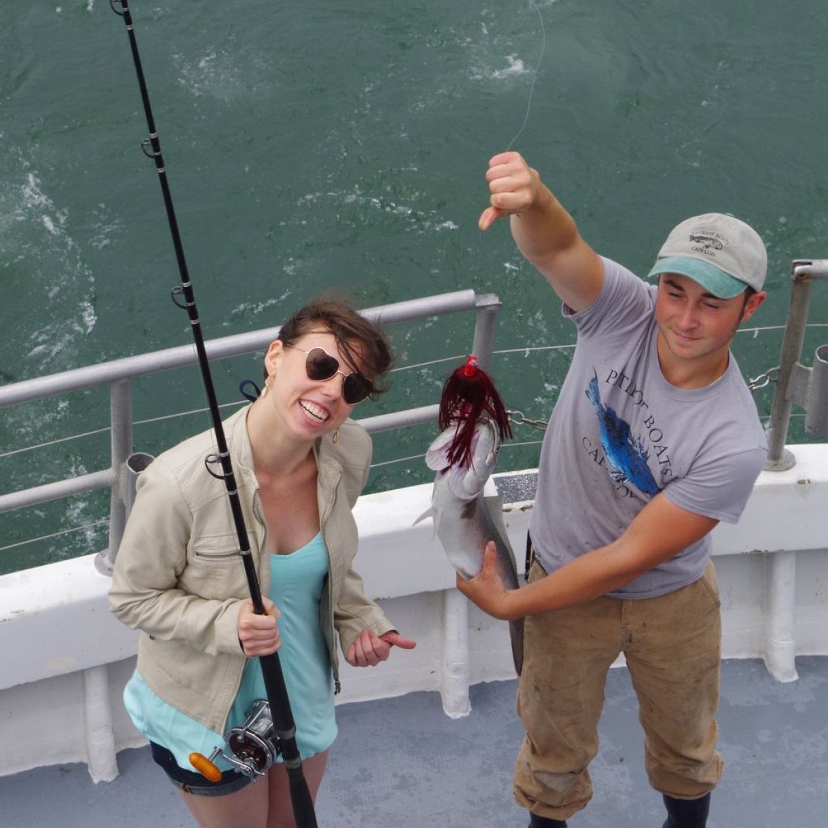 Two people on a boat, one holding a fishing rod, the other displaying a caught fish.