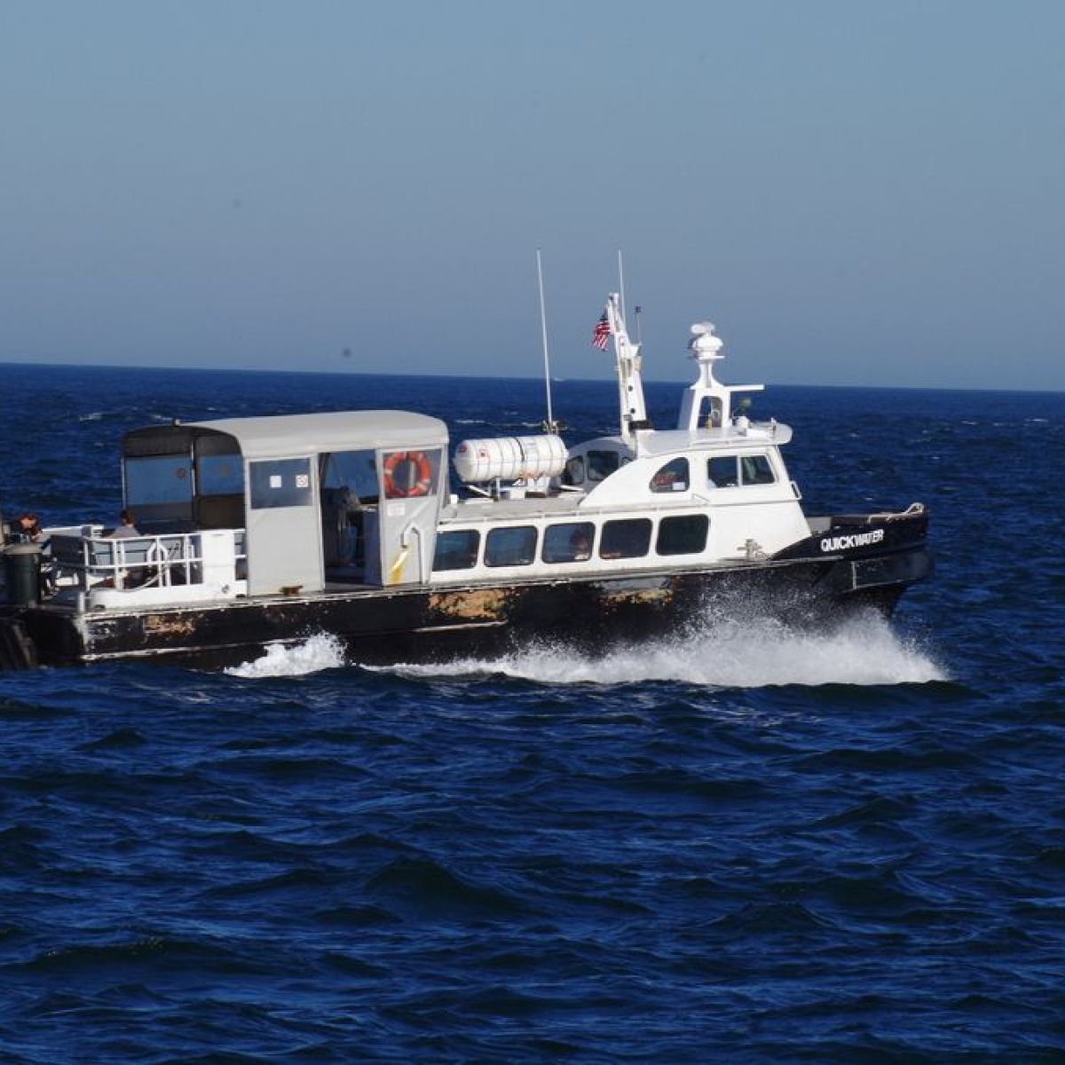 Small boat with cabin cruising in blue ocean under clear sky.