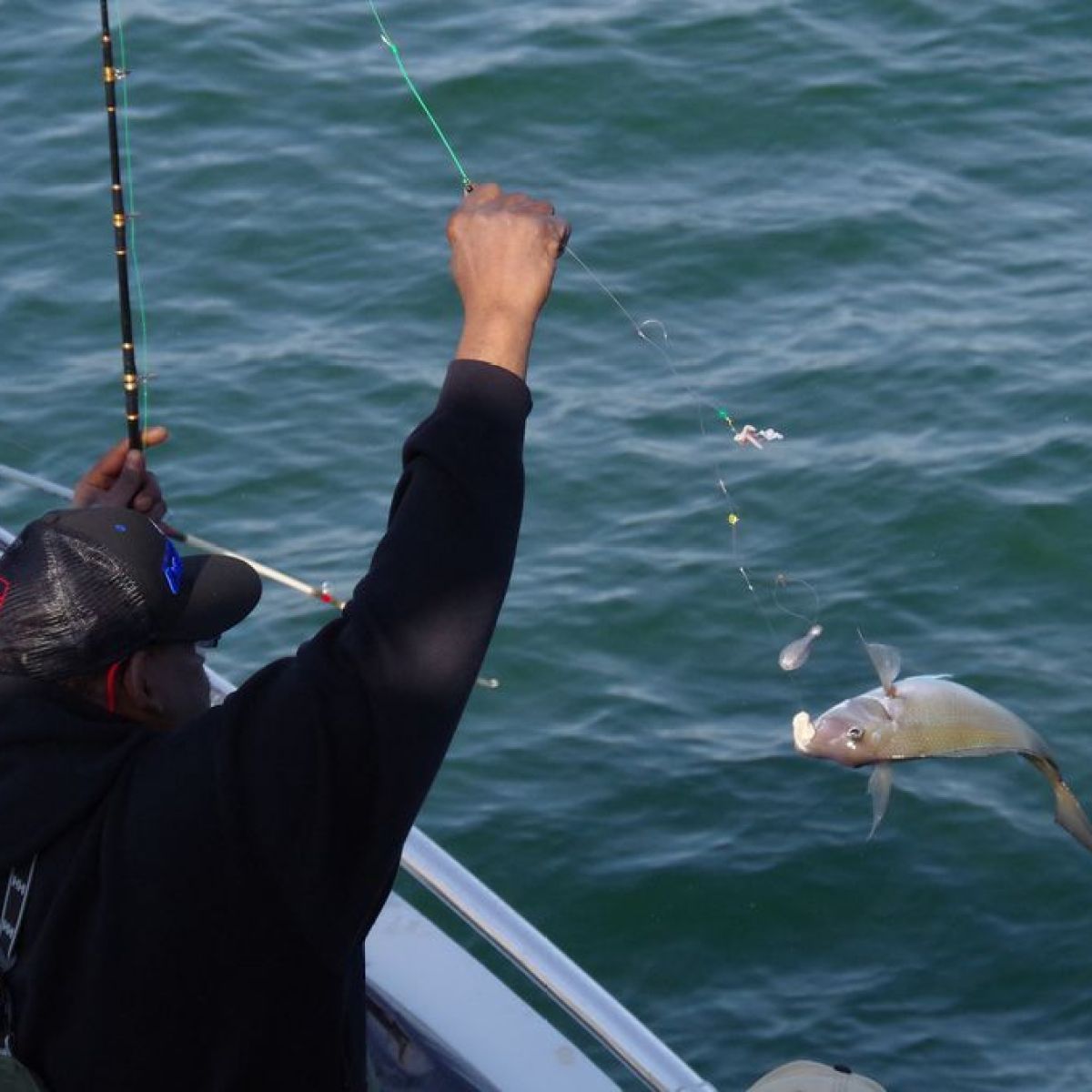 Two people fishing on a boat; one holds a caught fish above the water.