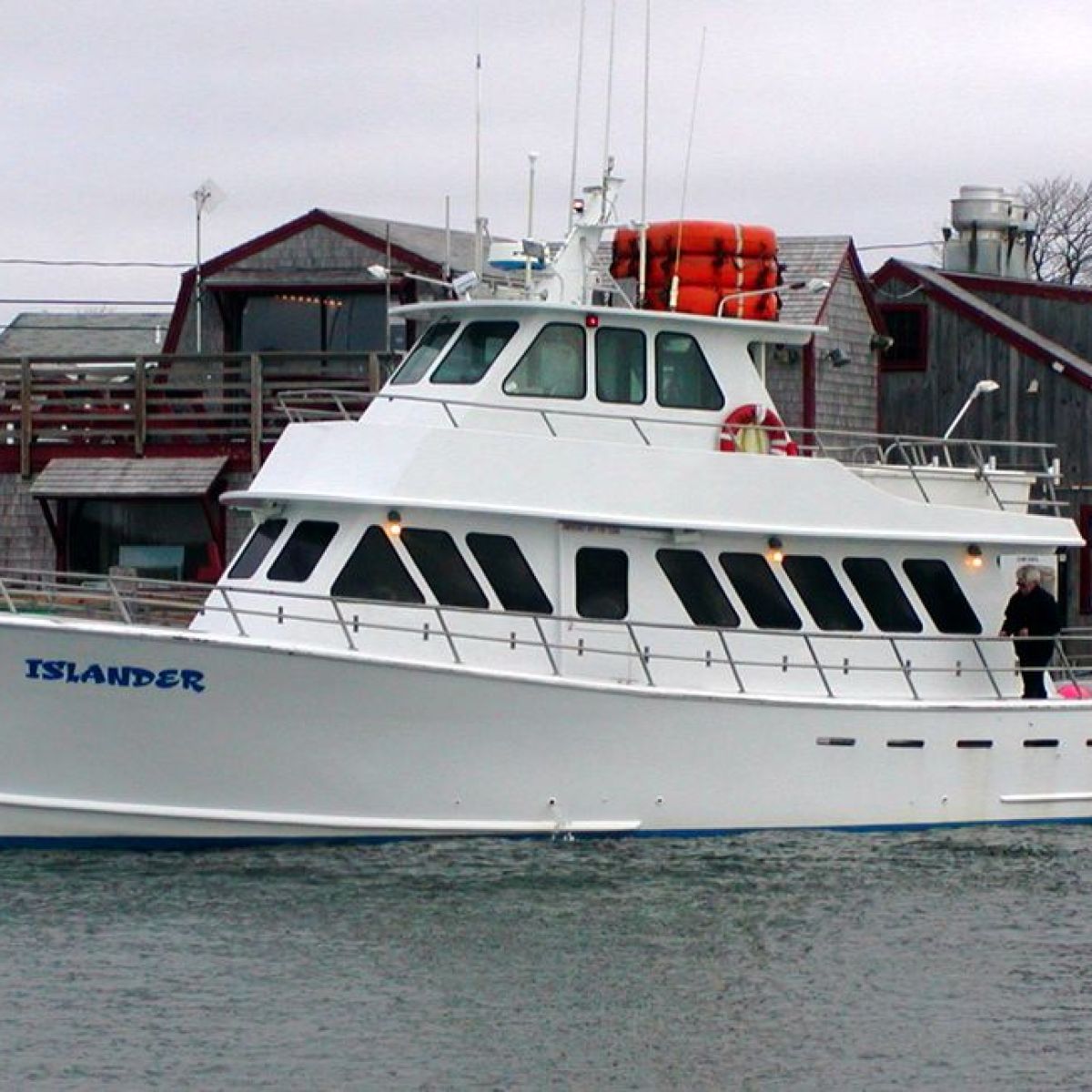 White fishing boat named Islander docked near wooden buildings.