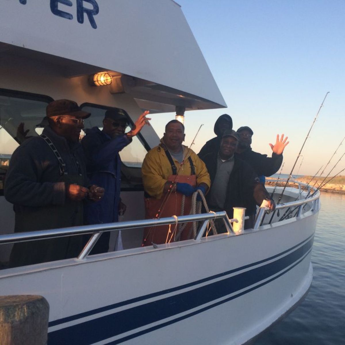 Group of people waving from a boat docked at a pier.