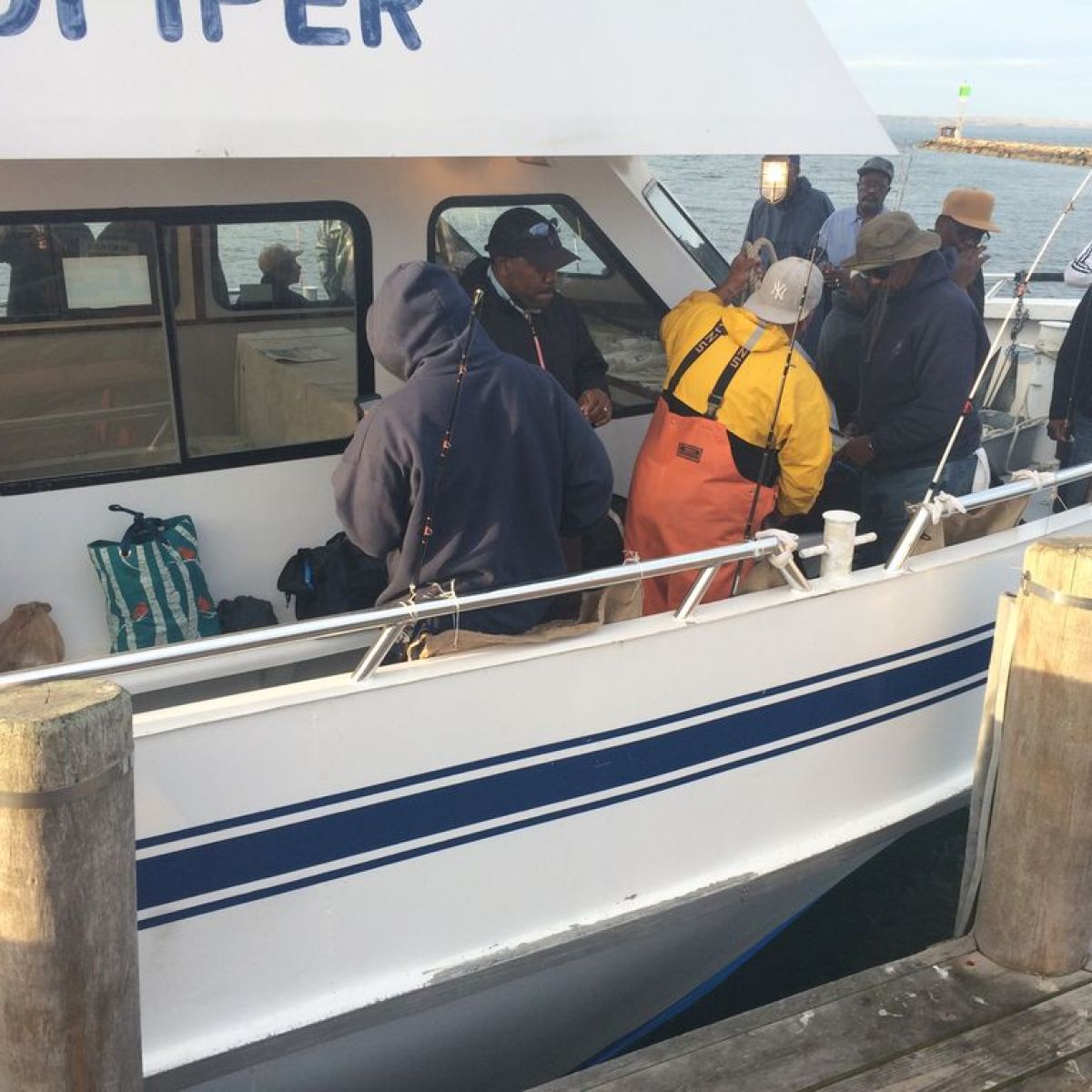 People in hoodies on a docked fishing boat with fishing rods.