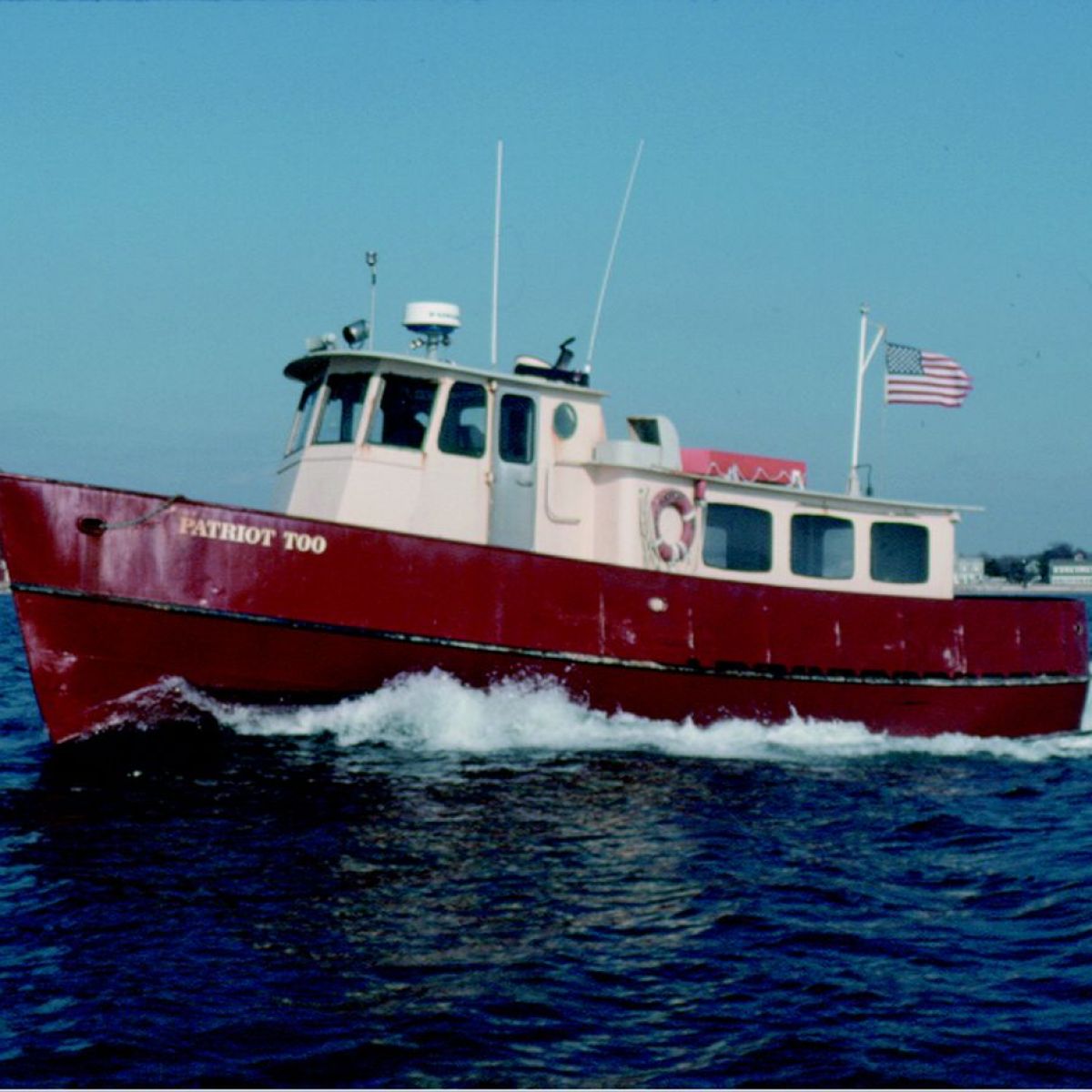 Red and white boat named 'Patriot Too' on water with American flag.