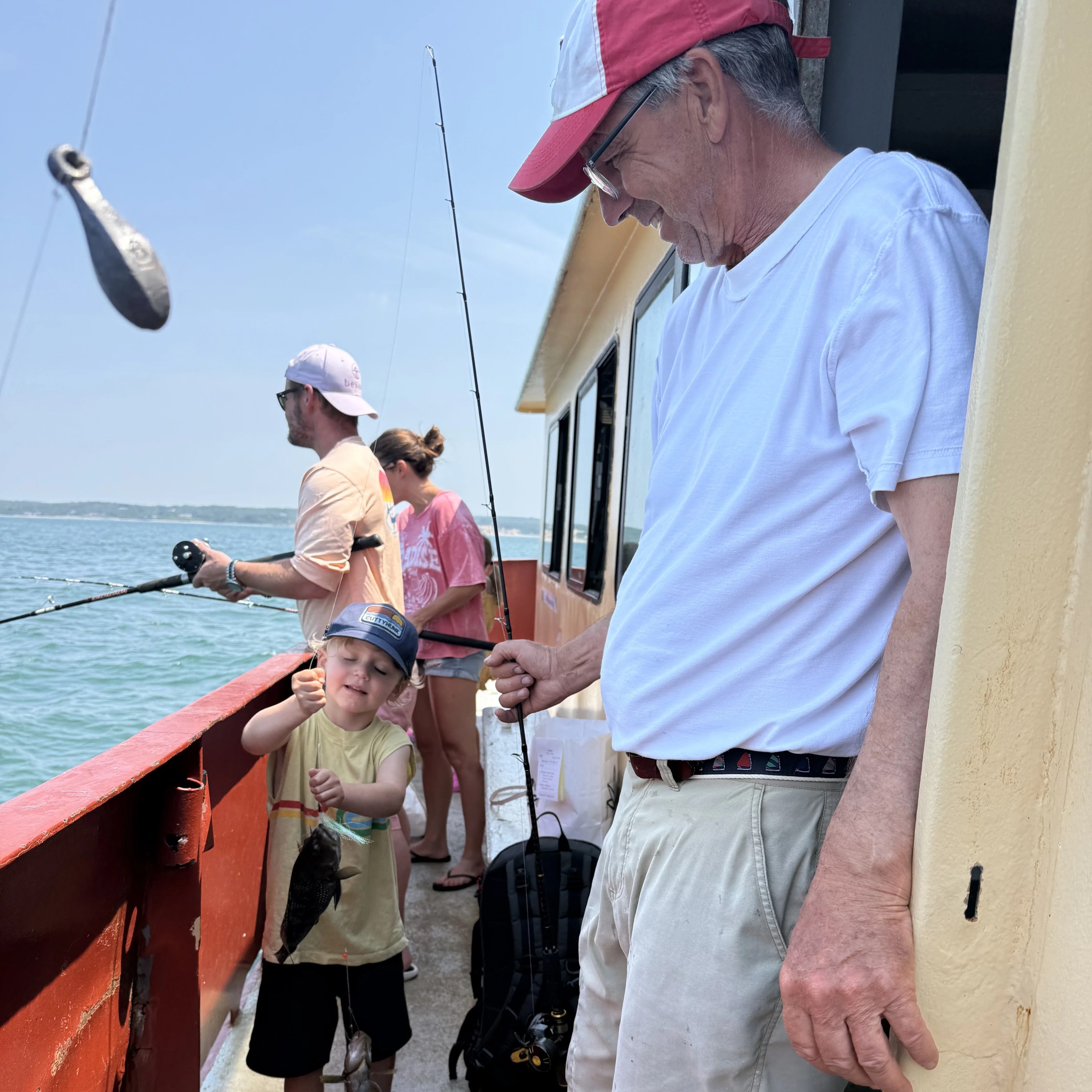 Man and child fishing on a boat, child holds a fish.